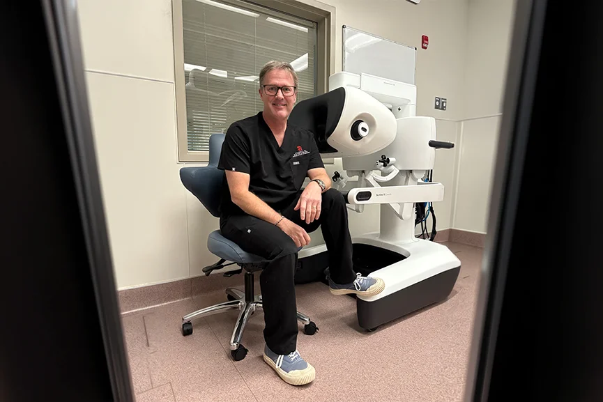 Doctor sitting next to a robotic-assisted surgery console in a medical facility.
