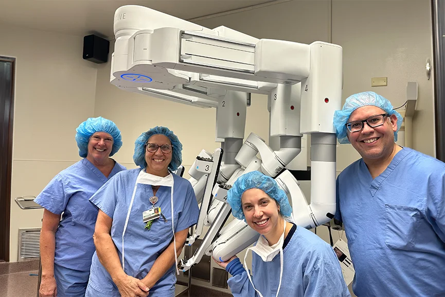 Surgical team standing beside a robotic surgery system in a hospital operating room.
