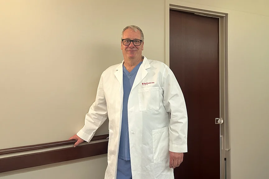Experienced surgeon standing in a clinic hallway wearing a white coat.